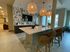 Stylish apartment lounge with a modern kitchen island, wicker bar stools, and decorative lighting.