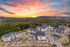 Aerial view of a modern apartment complex surrounded by lush greenery and a vibrant sunset sky.