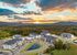 Aerial view of modern apartment complex surrounded by lush greenery and hills at sunset.