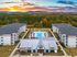 Aerial view of a modern apartment complex with three buildings surrounding a large swimming pool, set against a scenic sunset backdrop.