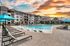 Modern apartment complex with a sparkling pool and vibrant sunset sky.