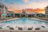Inviting poolside view at a modern apartment complex with lounge chairs and vibrant umbrellas during sunset.