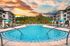Stunning outdoor pool area with turquoise umbrellas and modern apartment buildings under a vibrant sunset sky.
