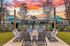 Inviting patio with a cozy fire pit surrounded by modern chairs, vibrant umbrellas, and a stunning sunset backdrop.
