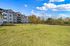 Serene view of modern apartments with lush green space and vibrant trees under a clear blue sky.
