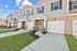 Huntsville, AL, Pet-Friendly Townhouses - Elio at Research Park - Row of Attached Garages and Covered Entries With Brick Facade, Sidewalks, Fresh Landscaping Beds, and Open Sky Views.