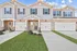 Dog-Friendly Townhouses in Huntsville, AL - Elio at Research Park - Townhome Exterior With Brick and Gray Siding, Attached Garages, Concrete Driveways, and Manicured Lawn Under Blue Sky.