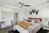 Townhouses in Huntsville, AL - Elio at Research Park - Spacious Bedroom With Tray Ceiling, Ceiling Fan, Wooden Bed Frame, Desk, Nightstands With Lamps, Swivel Chair, and Soft Neutral Decor.