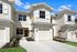 Charming townhouse with a modern facade, featuring a pristine driveway and elegant landscaping under a clear blue sky.