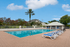 Luxurious outdoor swimming pool area with stylish sun loungers, surrounded by lush greenery and a charming clubhouse in the background.