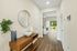 Bright hallway with elegant decor, featuring a stylish wooden console, large mirror, and leading to a light-filled living room with a scenic garden view.
