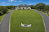Elegant clubhouse surrounded by lush greenery, framed by a winding driveway under a clear blue sky.