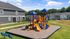 Inviting playground set within a vibrant community, showcasing modern townhouses and lush green space under a bright blue sky.