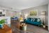 Inviting living area with chic teal sofa, vibrant pillows, and elegant decor, seamlessly connected to a modern dining space and open kitchen.