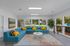 Bright and airy living space with a modern blue sectional sofa, colorful cushions, and expansive windows overlooking a lush garden.