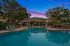Luxurious evening poolside view featuring a serene swimming pool, elegant lounge chairs, vibrant landscaping, and a charming clubhouse with ambient outdoor lighting.