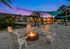 Charming outdoor fire pit area at sunset with cozy Adirondack chairs, overlooking serene apartment views.
