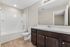 Modern bathroom showcasing a sleek white bathtub, elegant dark wood vanity, and spacious mirror, with stylish recessed lighting.