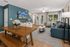Chic open-concept living room with elegant dining area, adorned with fresh flowers, plush blue sofa, and large windows inviting natural light.