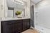 Elegant bathroom with stylish dark wood vanity, spacious mirror, and modern shower, accented by warm lighting and decorative plant.