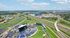 Stunning aerial view of a vibrant cityscape featuring a large outdoor amphitheater, intertwined highways, and lush green spaces under a blue sky.