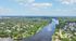 Breathtaking aerial view of a vibrant neighborhood by a serene river, surrounded by lush greenery and under a clear blue sky.