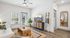Bright and modern living room with sleek ceiling fan, cozy white sofa, and elegant decor, featuring a large window and glass door leading to a serene outdoor view.