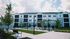 Modern apartment complex with elegant white and gray facade, featuring beautifully landscaped outdoor seating area with pergolas and lush greenery.